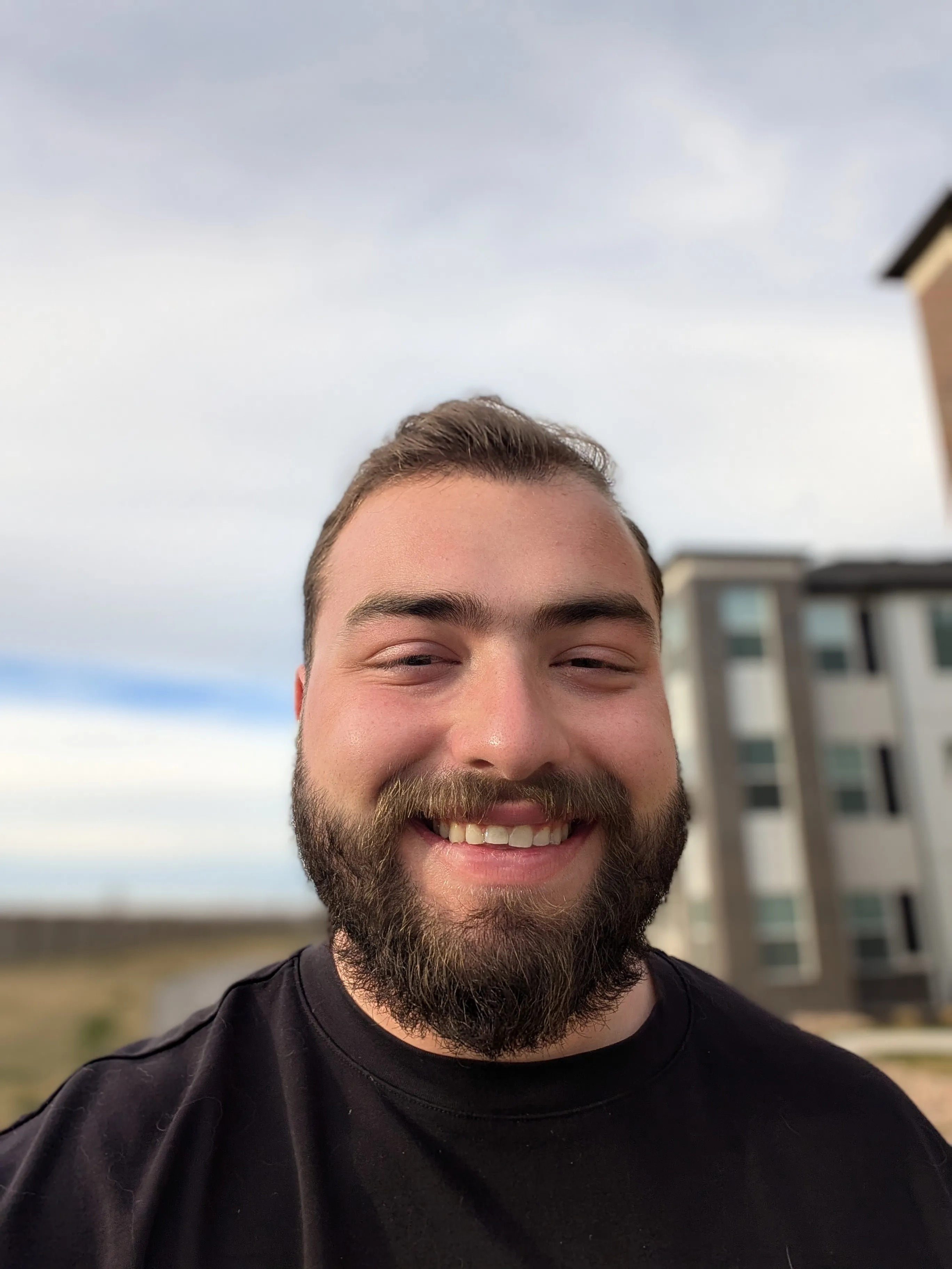 Denny Ninic, smiling, outdoors in front of an apartment building.